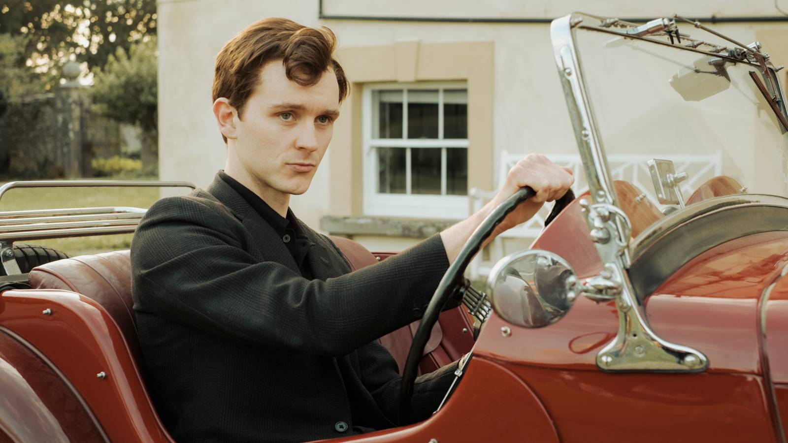 Richard dressed in black behind the wheel of a red convertible in Mr Burton