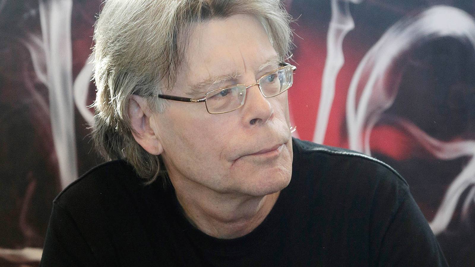 Stephen King looking to his left in front of Doctor Sleep cover art