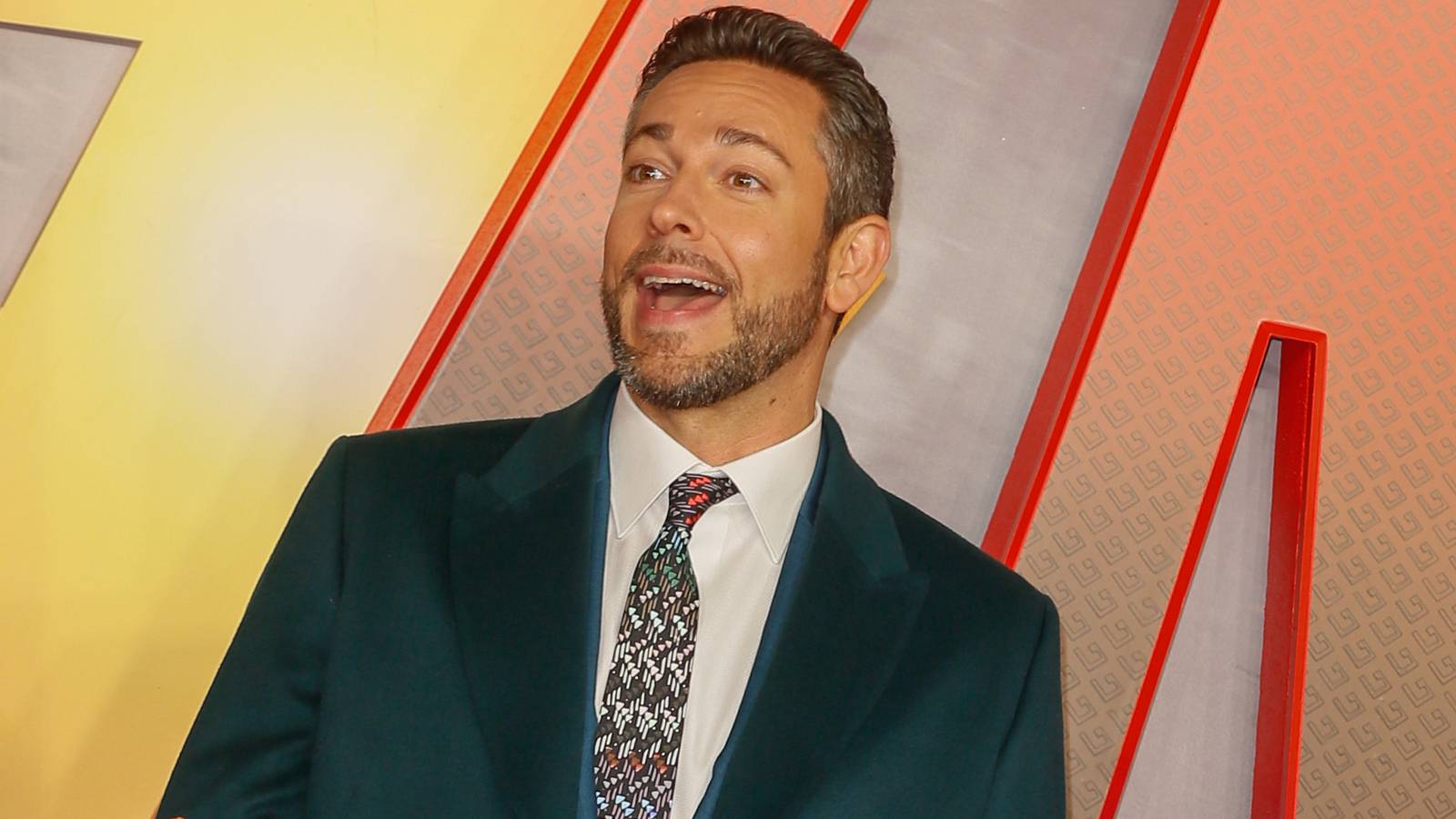 Zachary Levi smiling widely on a red carpet for Shazam