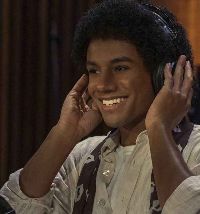 Jaafar Jackson as Michael Jackson smiling while wearing headphones in Michael